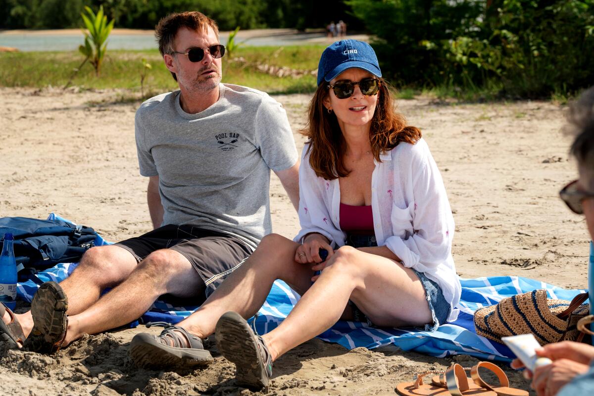 A man and a woman sit on a towel laid over sand