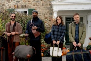 Three men and a woman stand while holding luggage