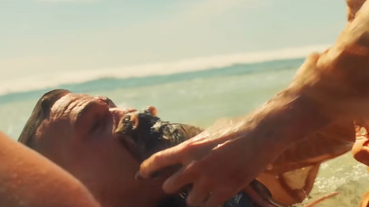 A man being force fed a rat on the beach in The Surfer