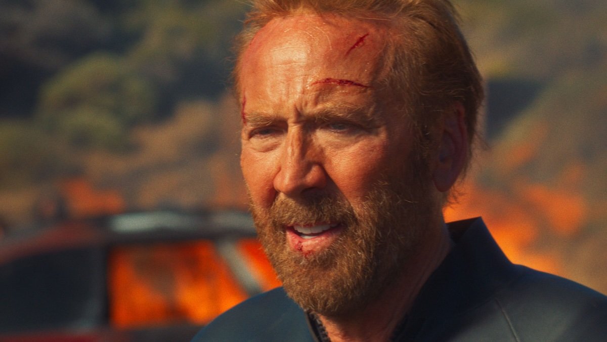 A sun burnt and bloodied Nic Cage on the beach in The Surfer