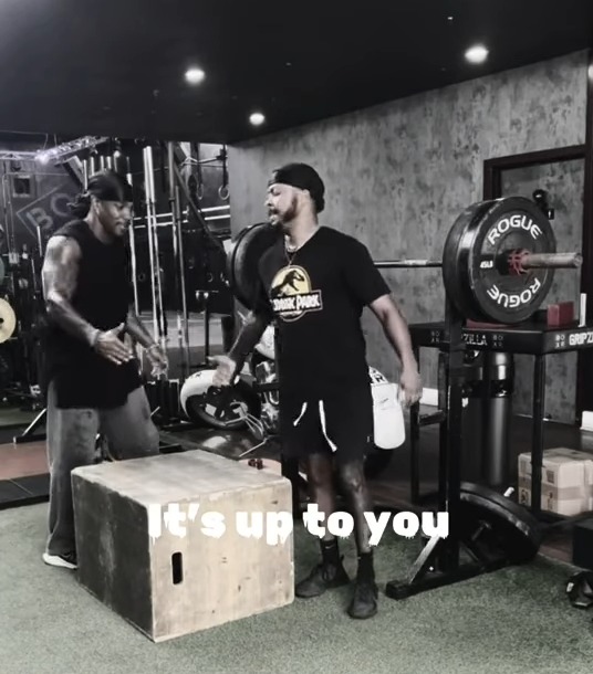 Two men in a gym, one holding a water bottle, with the text "It's up to you".