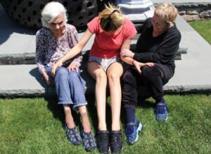 Three generations of women sitting together outdoors, wearing matching shoes.