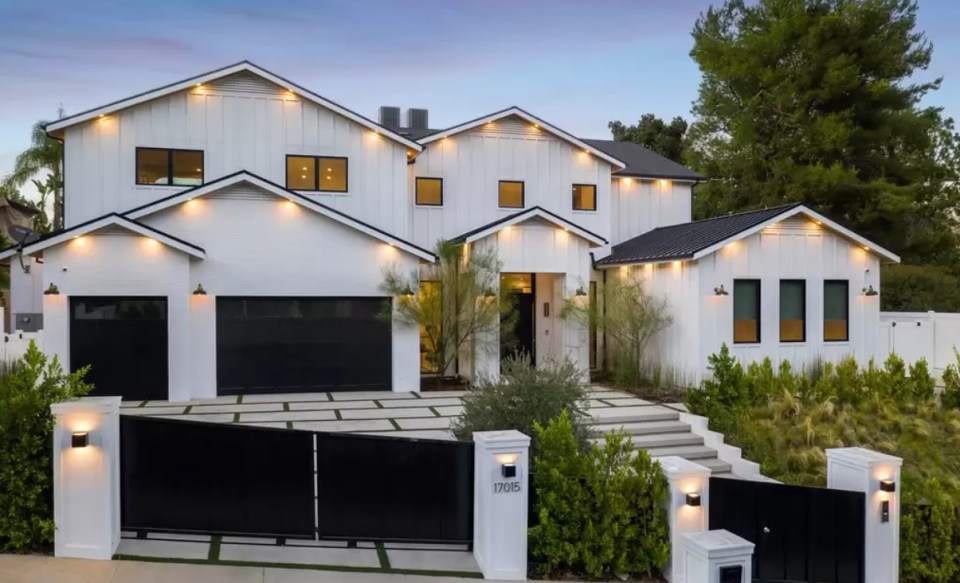 White farmhouse with black garage doors and gate.