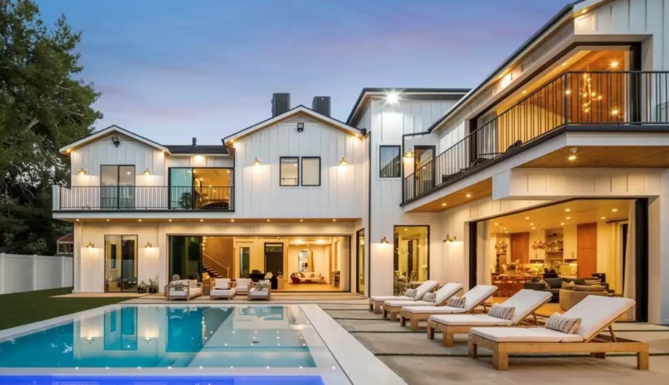 Large white farmhouse with pool and lounge chairs at dusk.