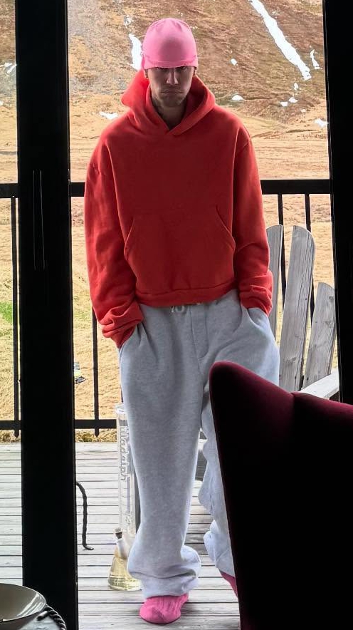 Justin Bieber wearing a pink cap, orange hoodie, and gray sweatpants.