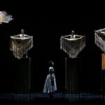 Two characters sing onstage as ghostly figures seem to hover above.
