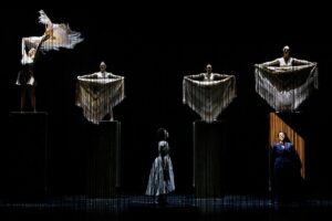 Two characters sing onstage as ghostly figures seem to hover above.