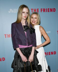 Kai Schreiber in a dark outfit and Naomi Watts in a white one stand in front of a backdrop