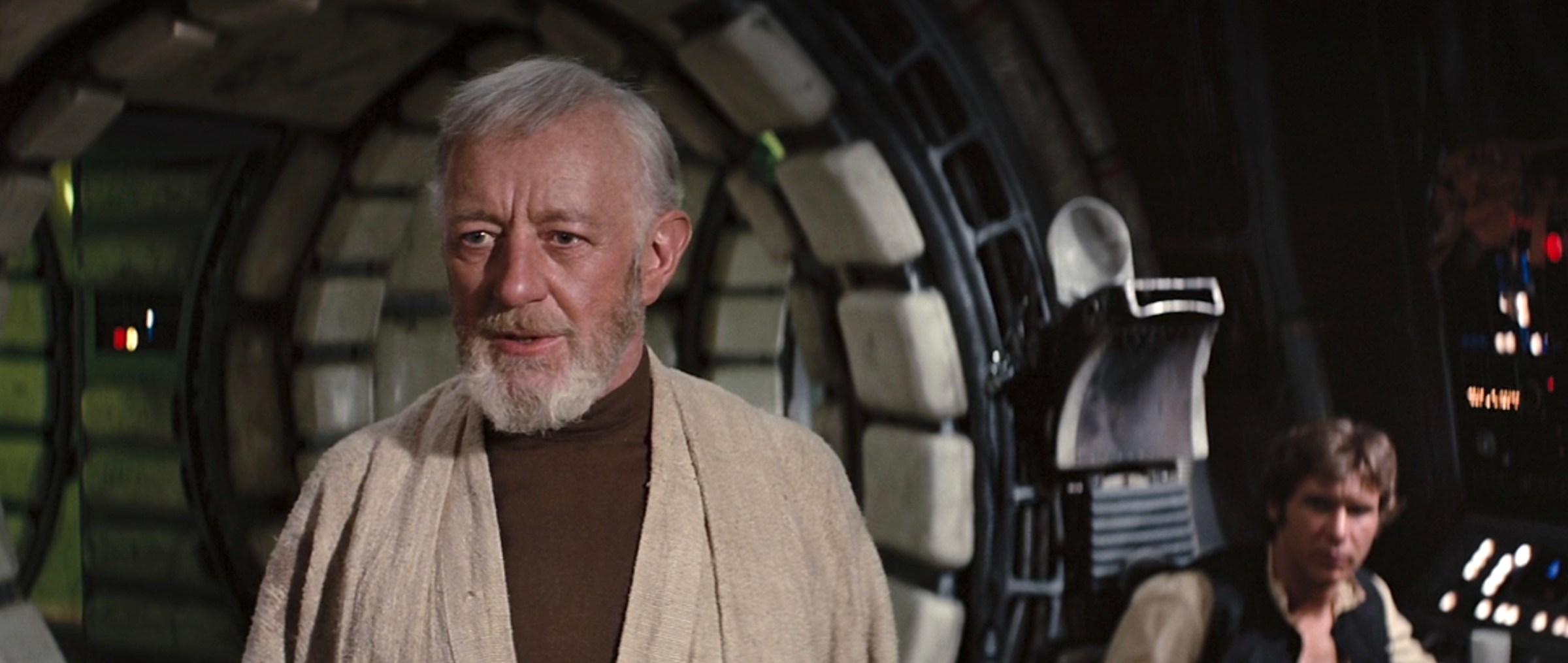 Alec Guinness as Obi-Wan Kenobi, standing in the Millennium Falcon with Han Solo (Harrison Ford) seated at a console in the background in Star Wars: Episode IV – A New Hope