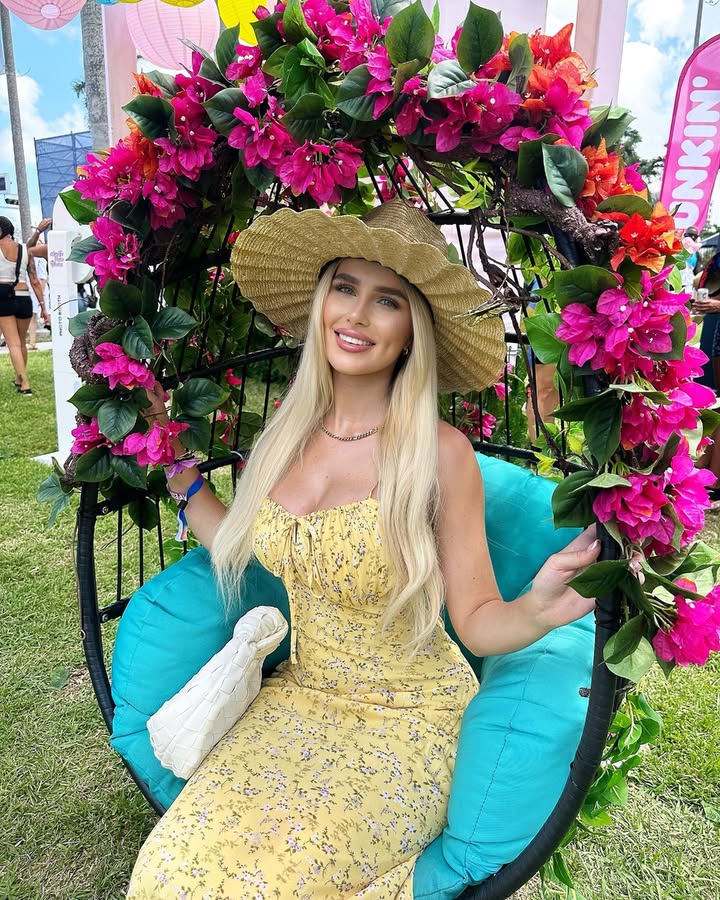 Woman in yellow floral dress sitting in a hanging chair decorated with pink flowers.