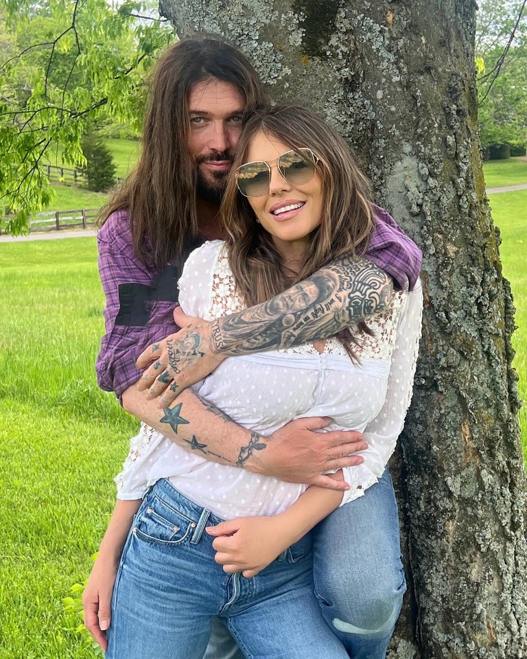 Liz Hurley and Billy Ray Cyrus embracing near a tree.
