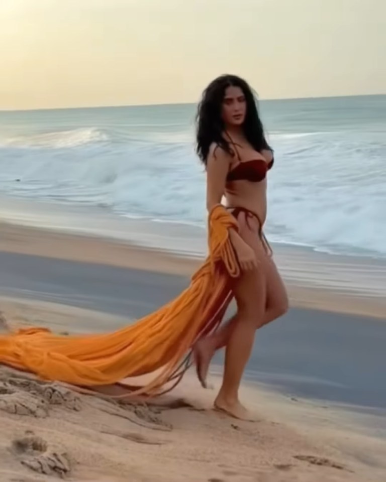 Salma Hayek in a red bikini and orange robe on a beach.