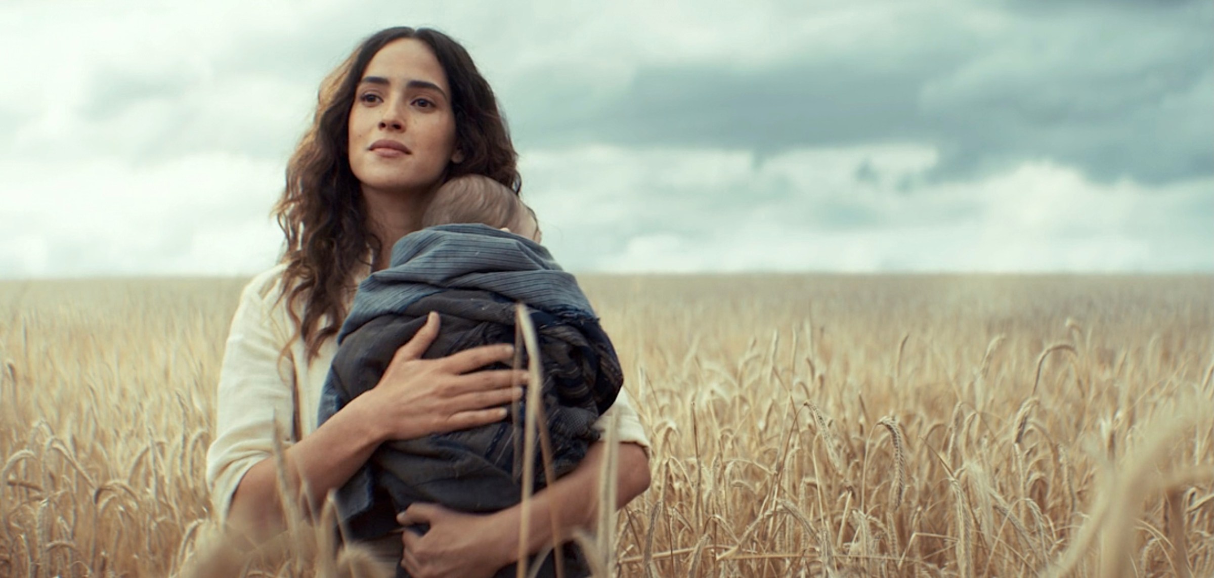 Bix (Adria Arjona) stands in a field of wheat, smiling and holding Cassian Andor’s young child in the final shot of Andor