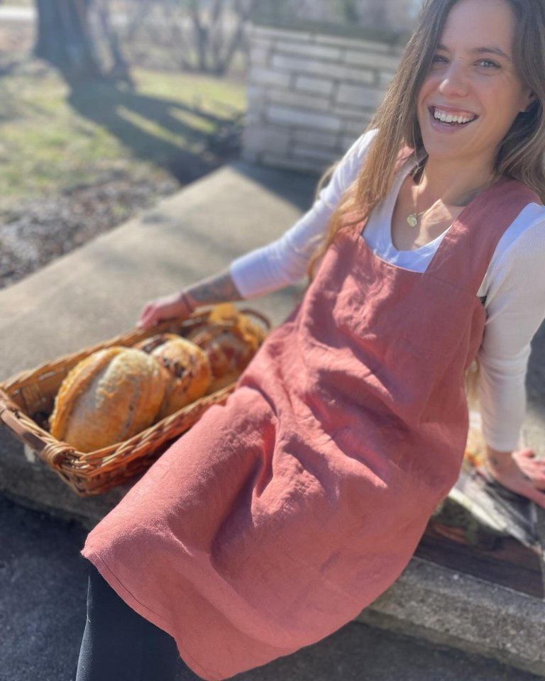 Woman in a pink apron holding a basket of bread.