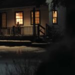 Joel from a distance seen sitting on his porch at night holding a guitar on The Last of Us