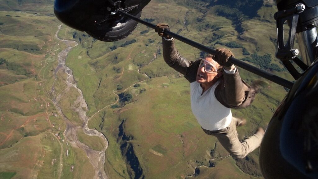 Tom Cruise hanging from a flying biplane high above the ground in Mission: Impossible - The Final Reckoning