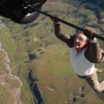 Tom Cruise hanging from a flying biplane high above the ground in Mission: Impossible - The Final Reckoning