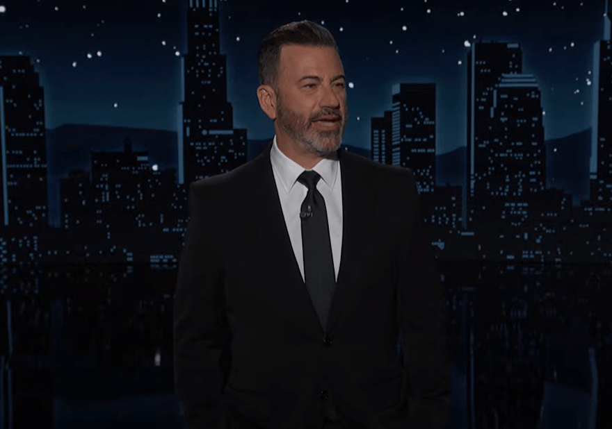 Jimmy Kimmel in a suit against a cityscape backdrop.