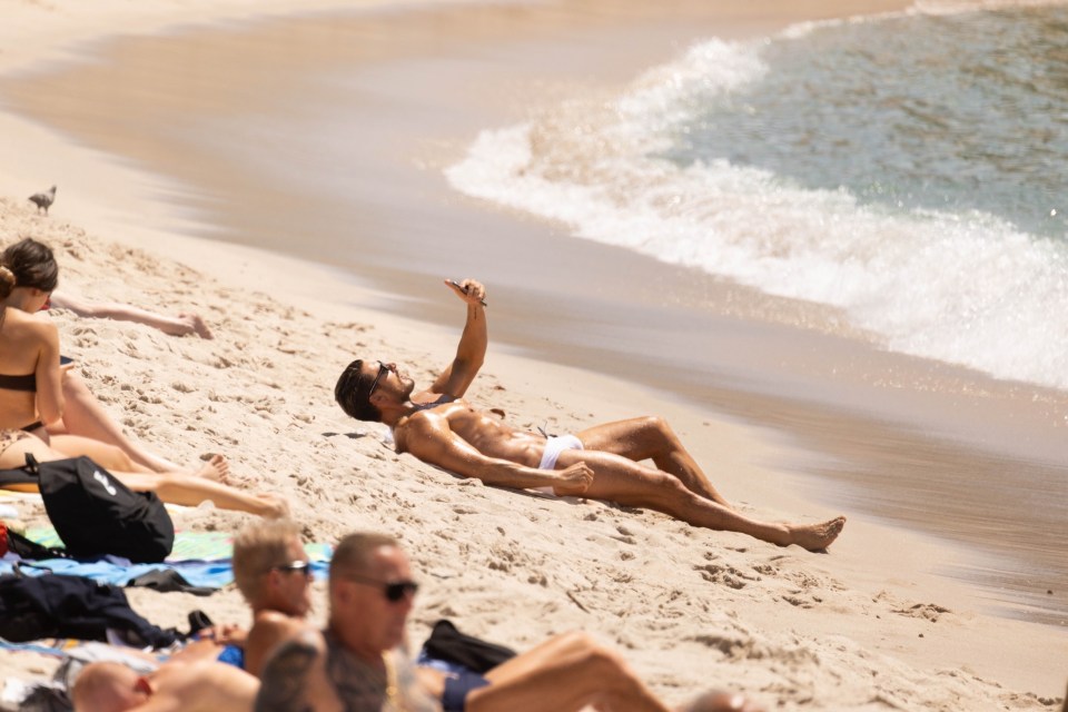 Hairstylist Chris Appleton sunbathing on a beach, using a phone.