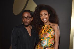 Kendrick Lamar and SZA stand in front of a backdrop with a Grammy trophy.