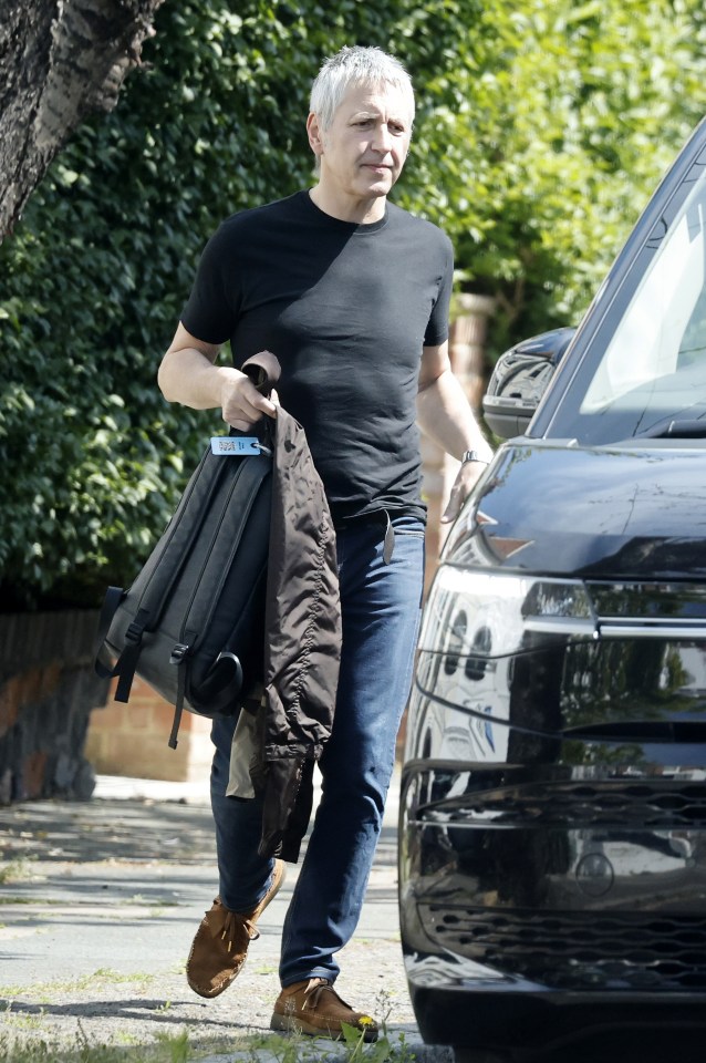 Noel Gallagher walking near a car.