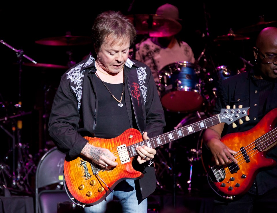 Rick Derringer performing on stage, playing an electric guitar.