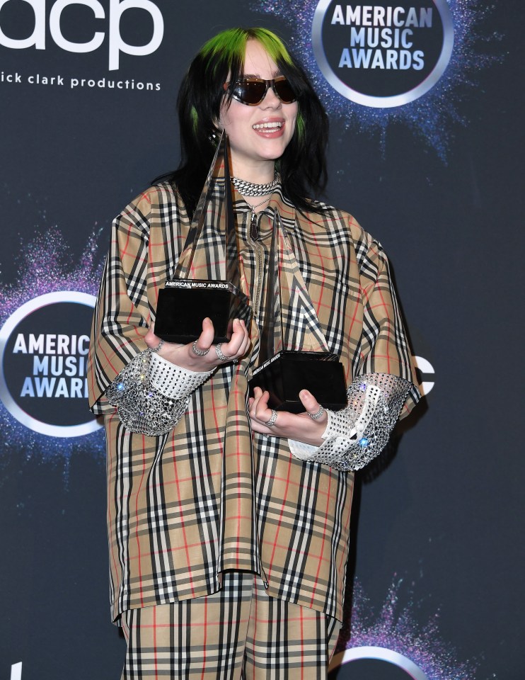 Billie Eilish at the American Music Awards, holding two awards.
