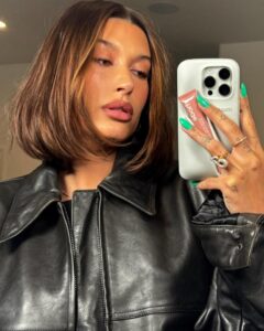 Hailey Bieber selfie holding rhode lip treatment.
