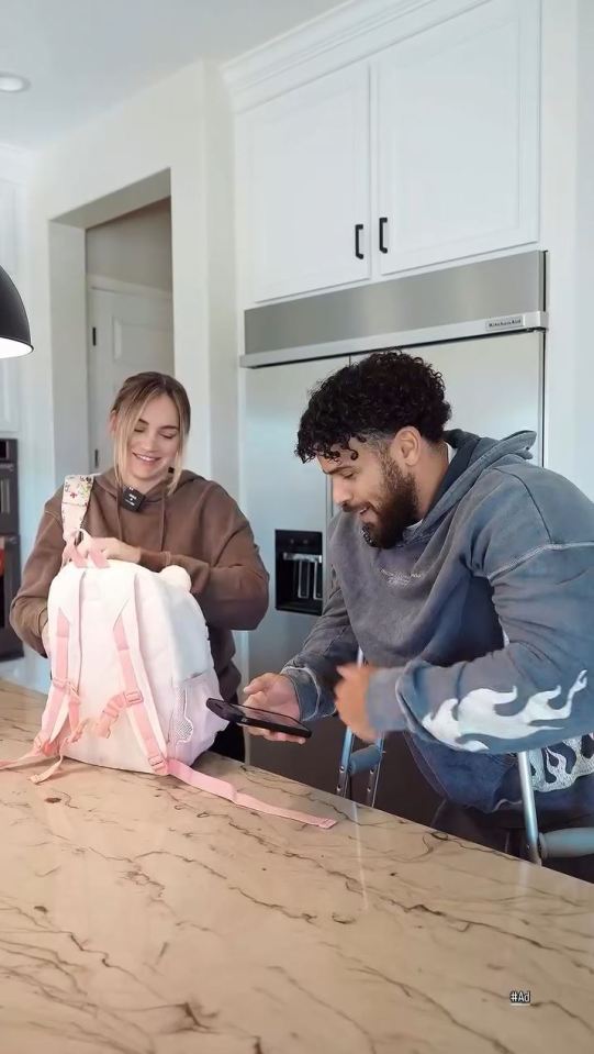 Couple packing a pink backpack in a kitchen.