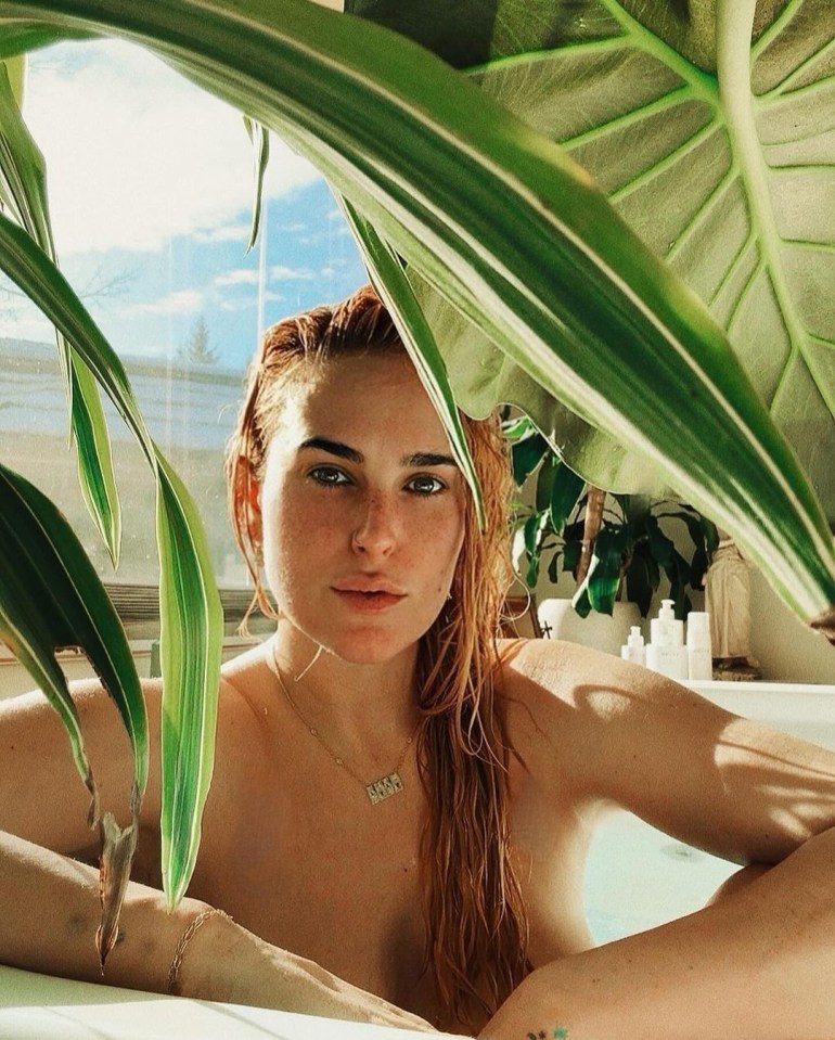 Rumer Willis in a bathtub, partially obscured by large green leaves.
