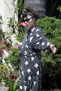 Toni Basil, singer of "Mickey," wearing a black and white geometric print robe, headscarf, sunglasses, and red lipstick.