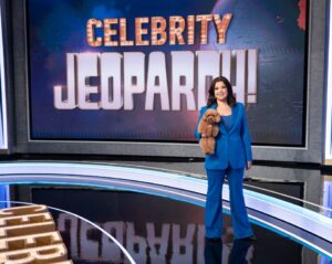 Ana Navarro on the set of Celebrity Jeopardy!, holding a small dog.