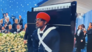 Andre 3000 wearing a baby grand piano to advertise his latest album 7 Piano Sketches