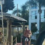 A shirtless man resembling Colin Farrell outside a coffee shop.
