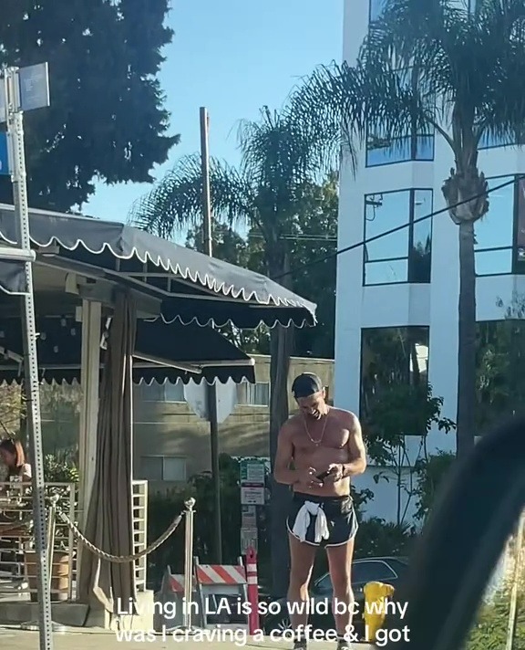 A shirtless man resembling Colin Farrell outside a coffee shop.