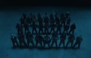 Screenshot of a music video showing a large group of shirtless men in silhouette.