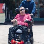 Tim Curry in a wheelchair, being pushed by another person.