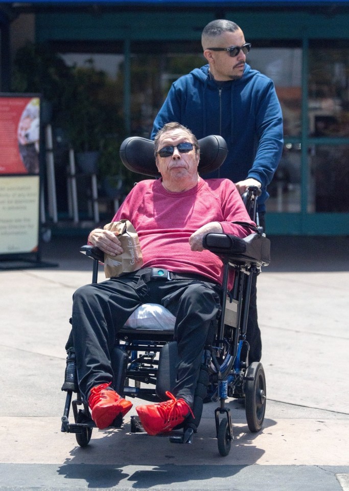 Tim Curry in a wheelchair, being pushed by another person.