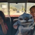 Maia Kealoha and Sydney Agudong ride in a truck as blue alien Stitch grabs the wheel in a still from 'Lilo & Stitch'.