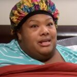 Woman in a floral shower cap and striped shirt speaks.