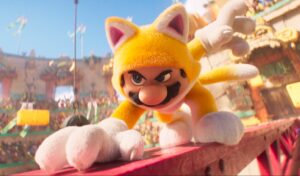 A man wearing a full body suit that makes him look like a fuzzy yellow cat and crouching on a steel beam in the middle of a colosseum.