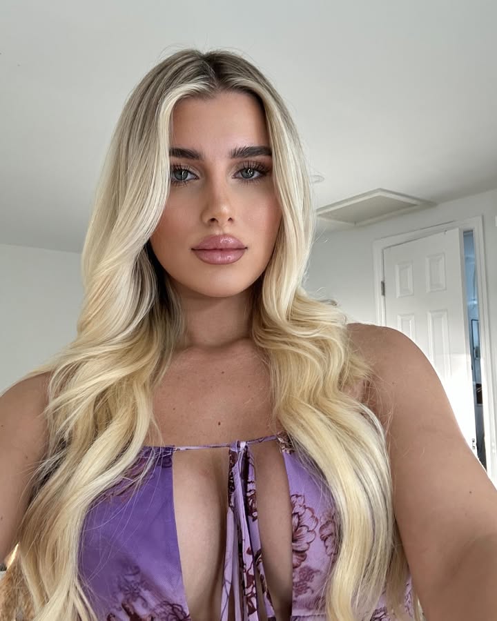 Woman with long blonde hair wearing a purple floral dress.