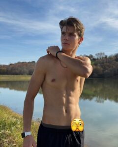 Shirtless young man standing by a lake.