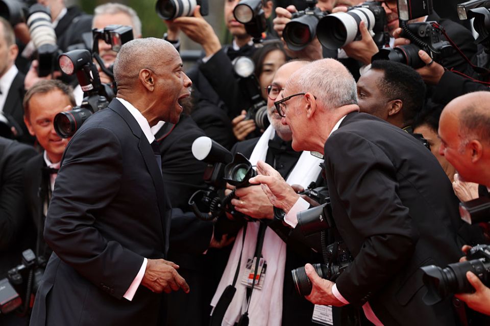 Denzel Washington speaking with a man amidst a throng of photographers.
