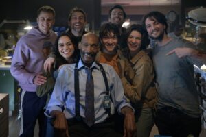 Tony Todd sitting on the set of Final Destination: Bloodlines, surrounded by the lead cast and directors Zach Lipovsky and Adam B. Stein, all smiling at the camera