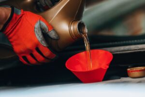 A gloved hand pouring motor oil into a red funnel.