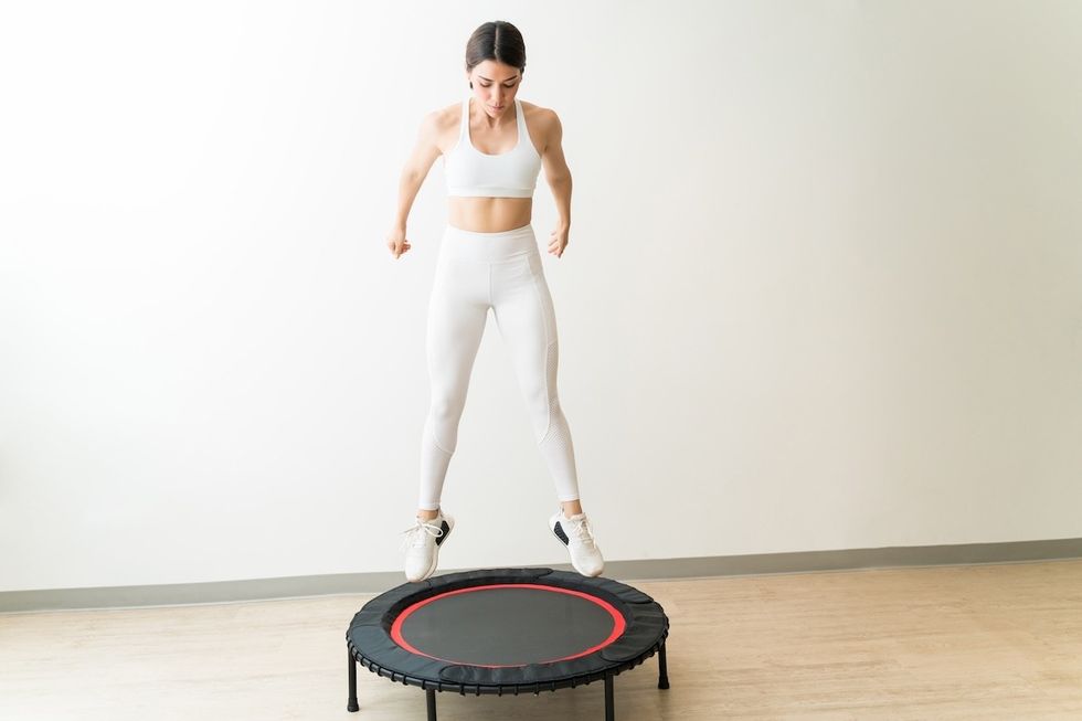 young woman in white workout gear jumping on a mini trampoline