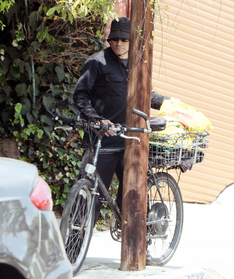 Crispin Glover riding a bicycle with a basket.