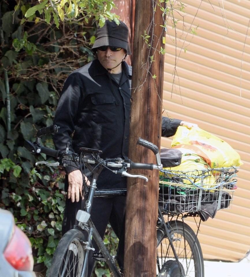 Crispin Glover on a bicycle with bags in the basket.
