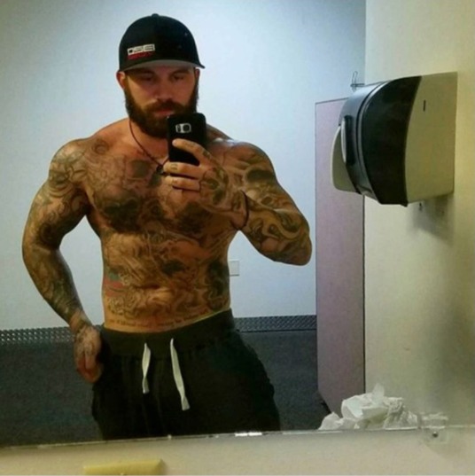 A shirtless tattooed man taking a selfie in a bathroom mirror.